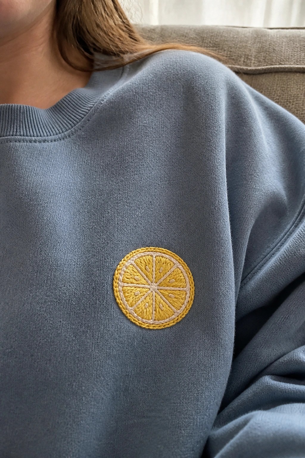 A blue sweatshirt with a yellow embroidered lemon slice on the chest.