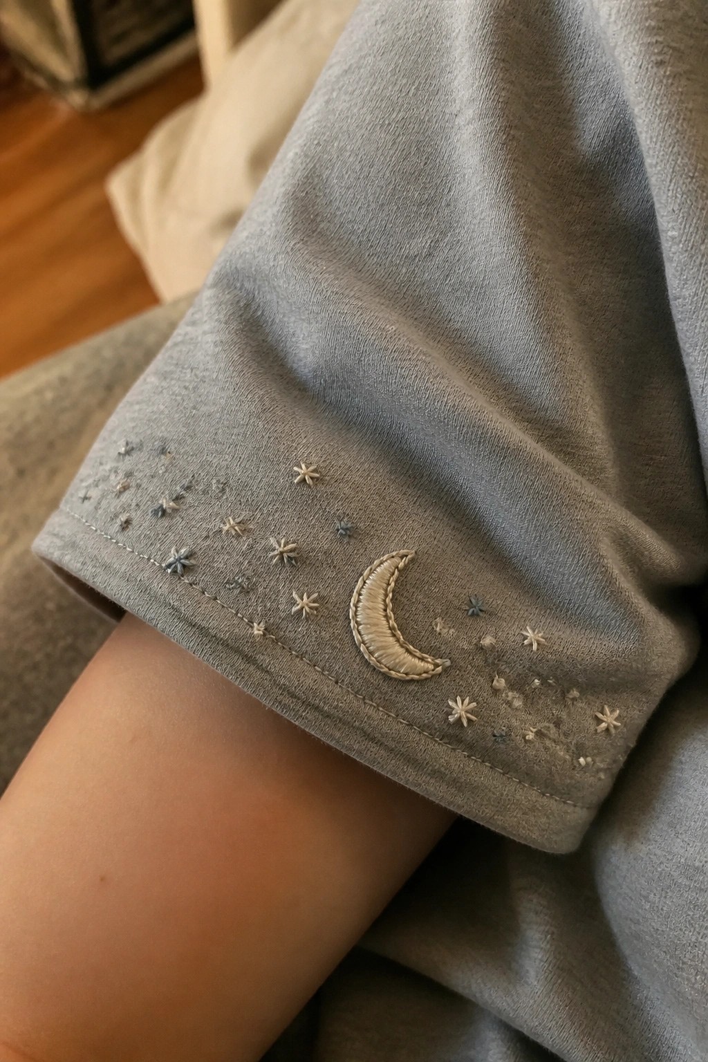 Gray t-shirt sleeve with beige crescent moon and scattered star embroidery.