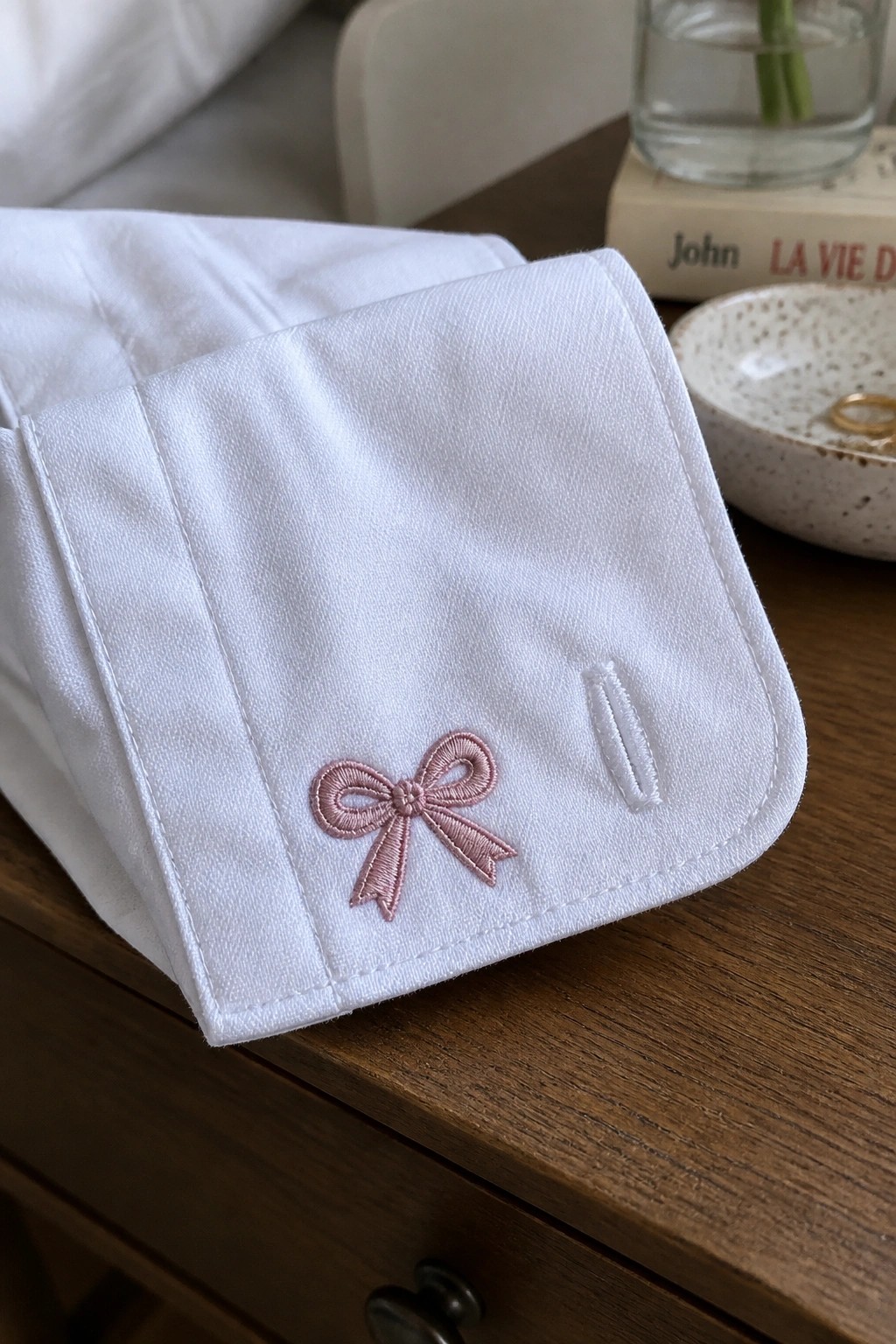 Close-up of a white shirt cuff with a small pink embroidered bow next to a buttonhole.