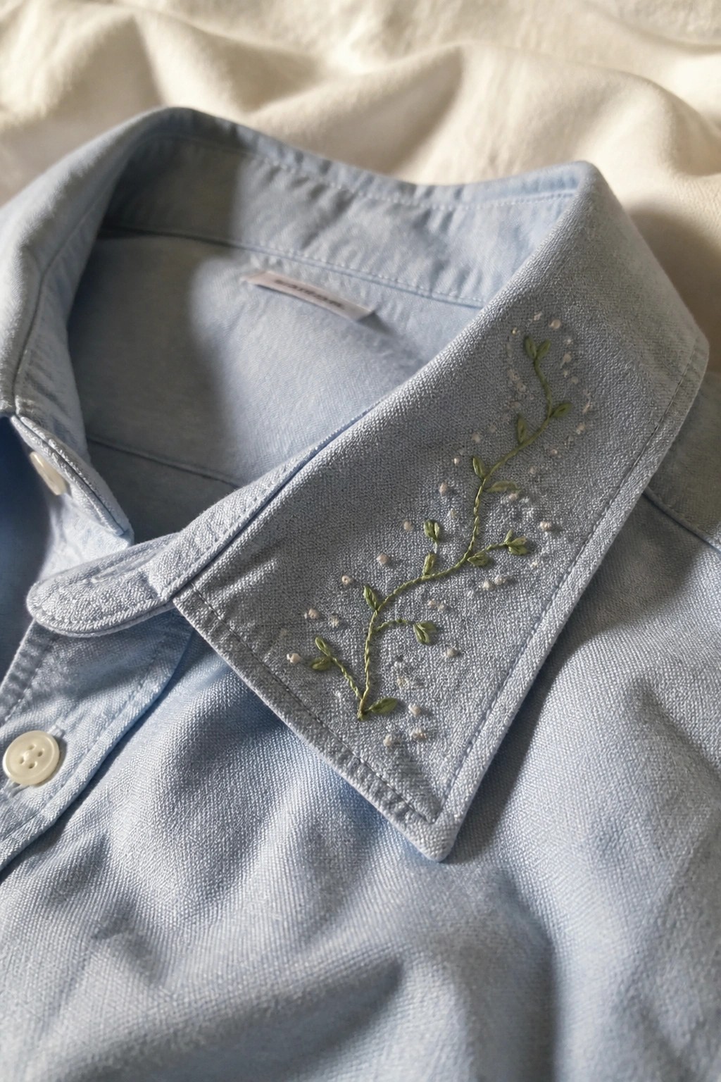 Light blue shirt collar with green vine embroidery and white dotted accents.