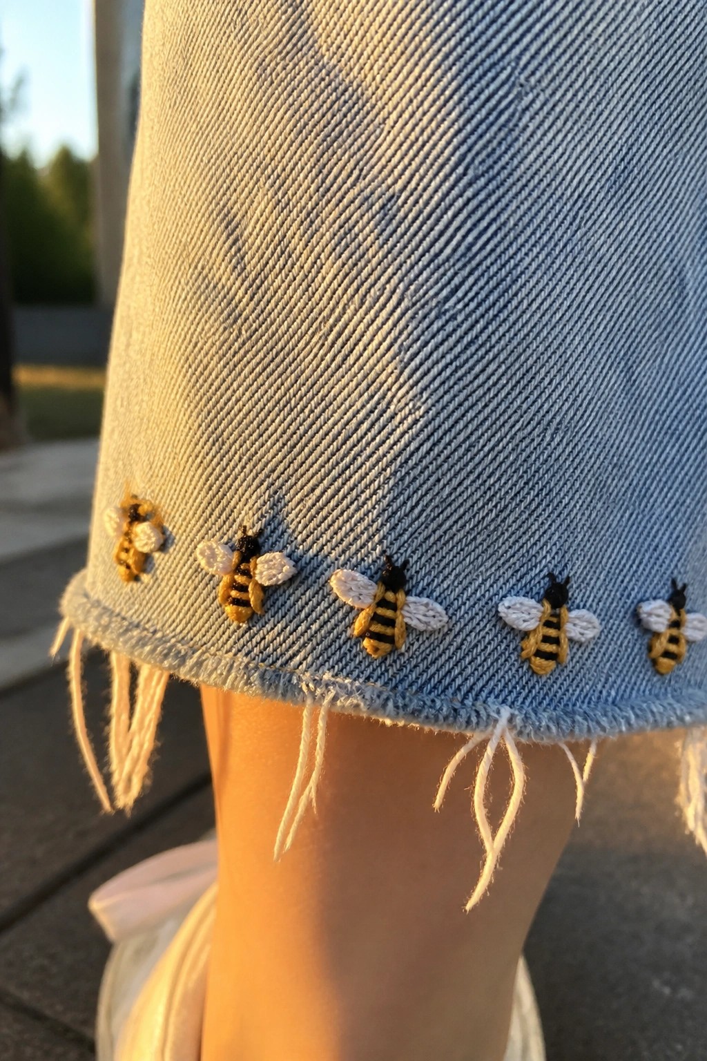 Light blue frayed denim hem embroidered with yellow and black bees in sunlight.