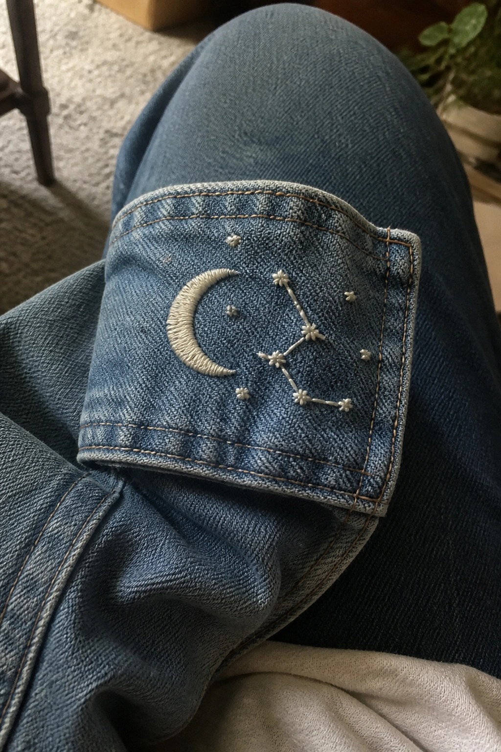 White embroidered crescent moon and constellation on a blue denim jeans pocket.
