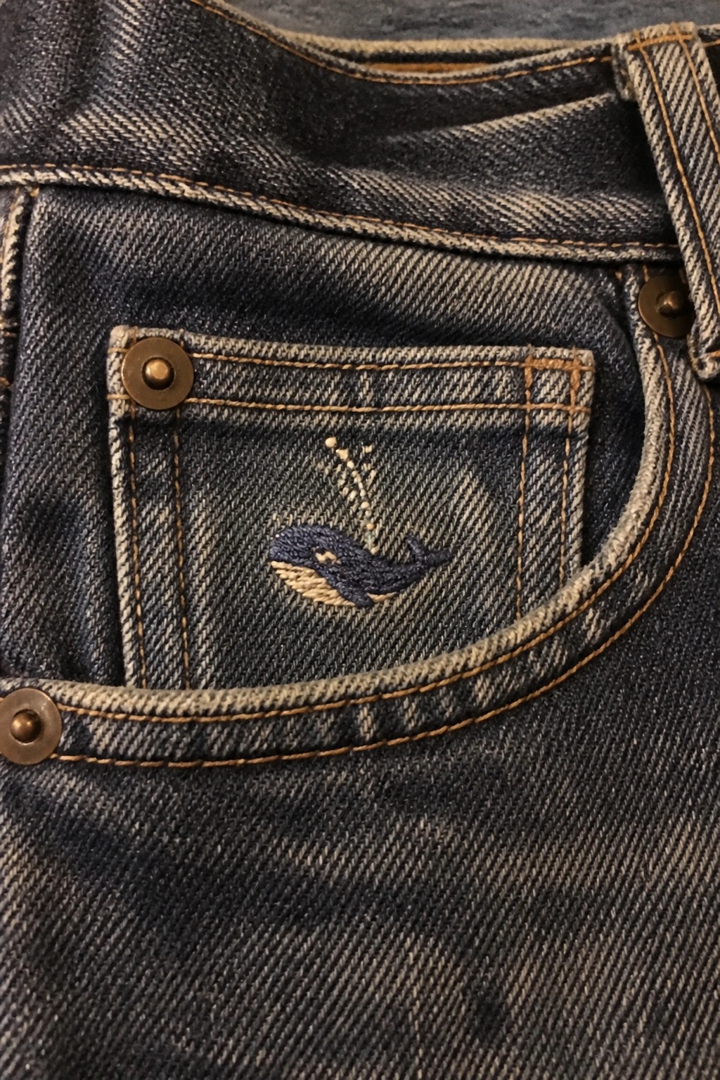 Embroidered blue whale with water spout stitches on a denim jeans pocket.