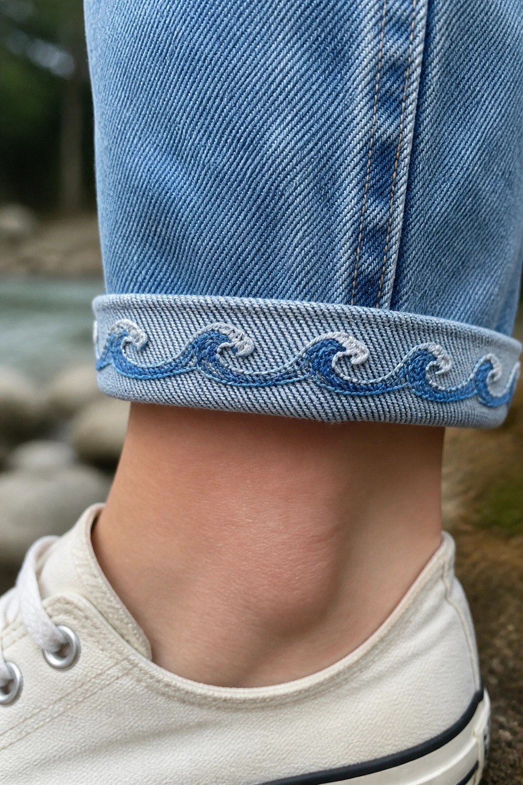 Cuffed light blue jeans with blue wave embroidery above white canvas sneaker
