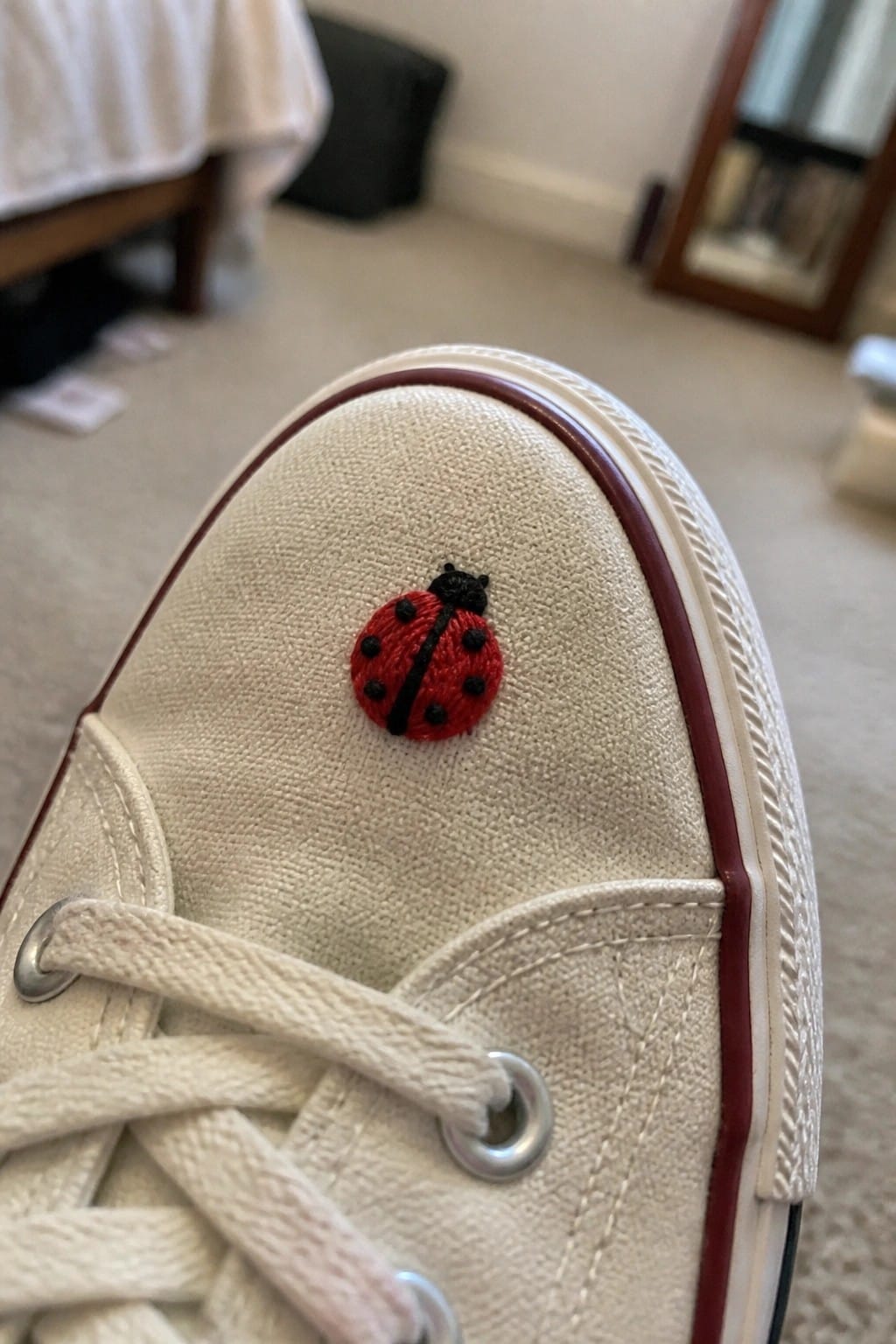 White canvas sneaker with embroidered red ladybug on the toe.