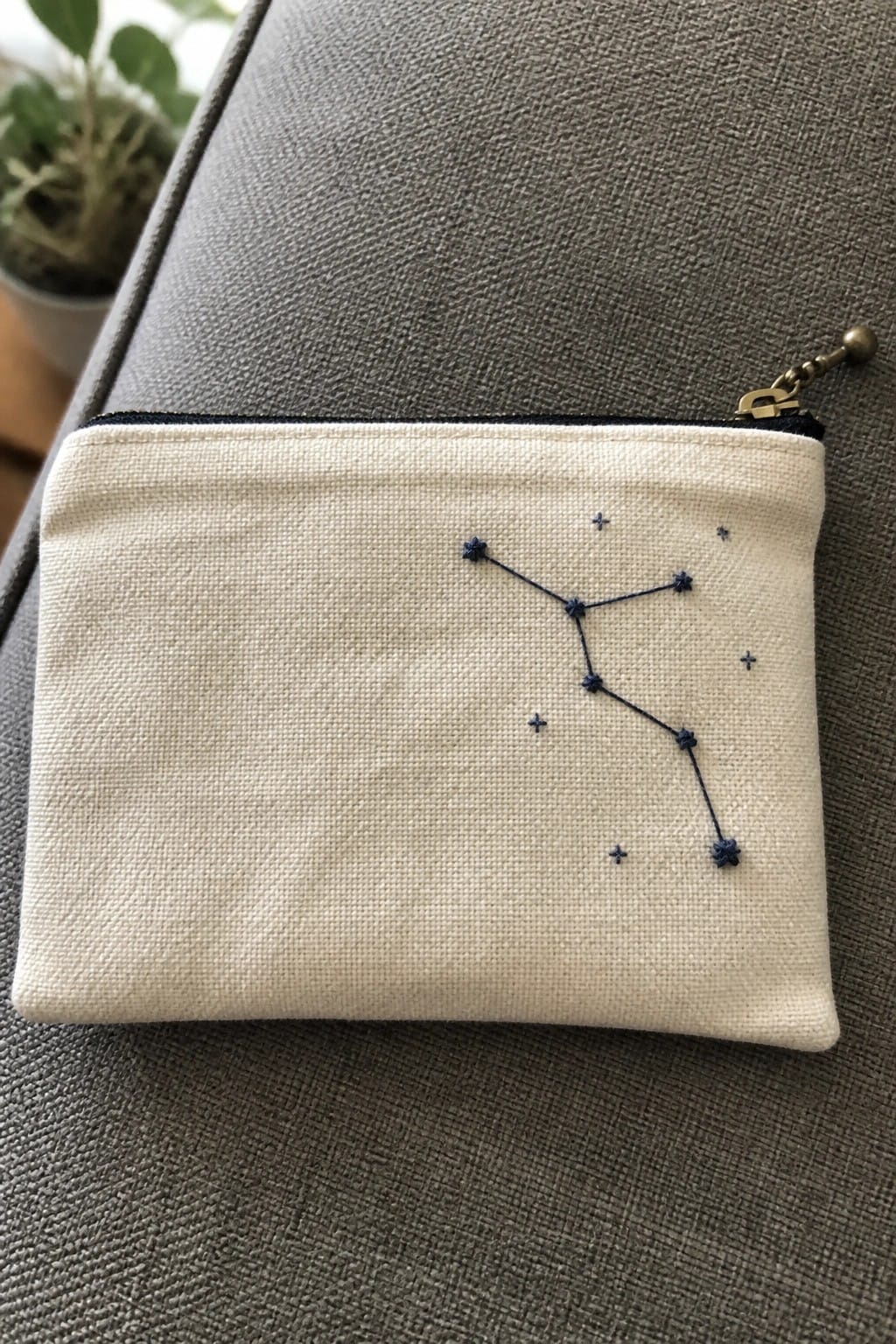 Cream-colored canvas pouch with embroidered sleeping fox on gray fabric.