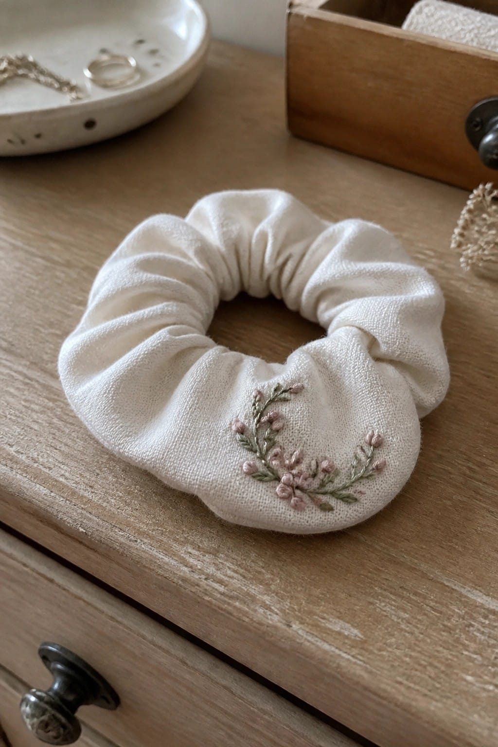 Embroidered cream scrunchie with pink florals on rustic wooden dresser.