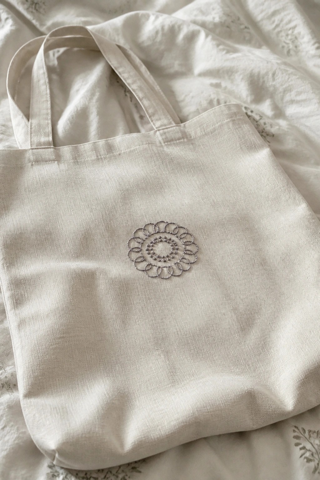 Cream canvas tote bag with silver floral embroidery on white linen.