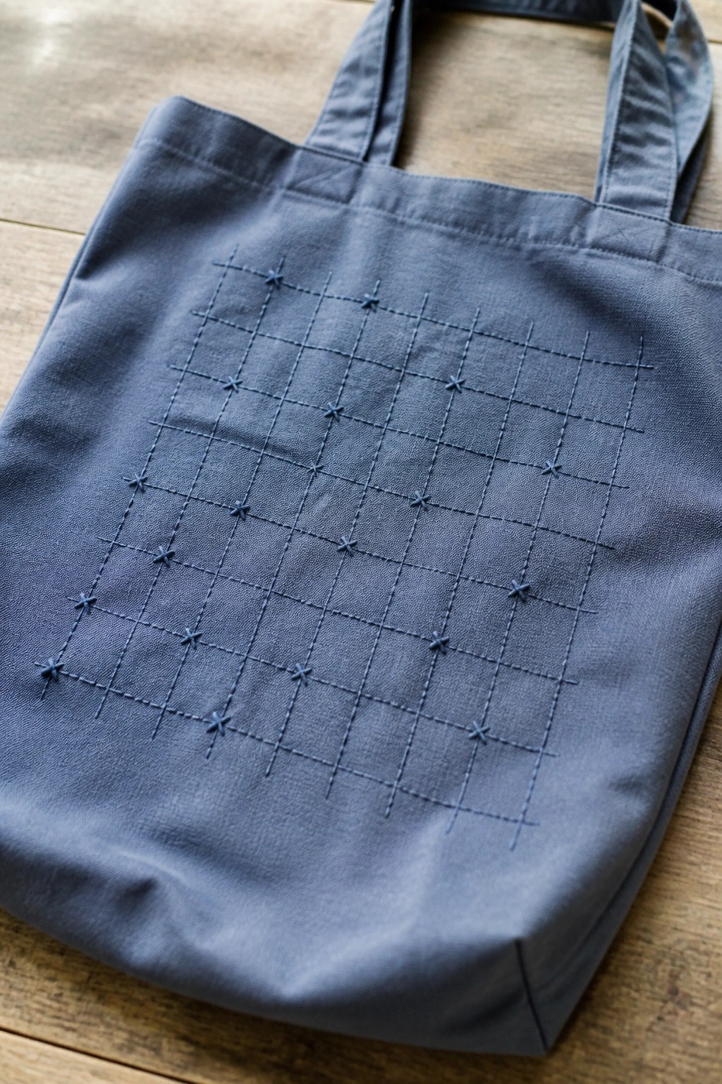 Blue tote bag with embroidered grid and cross stitches on wooden surface
