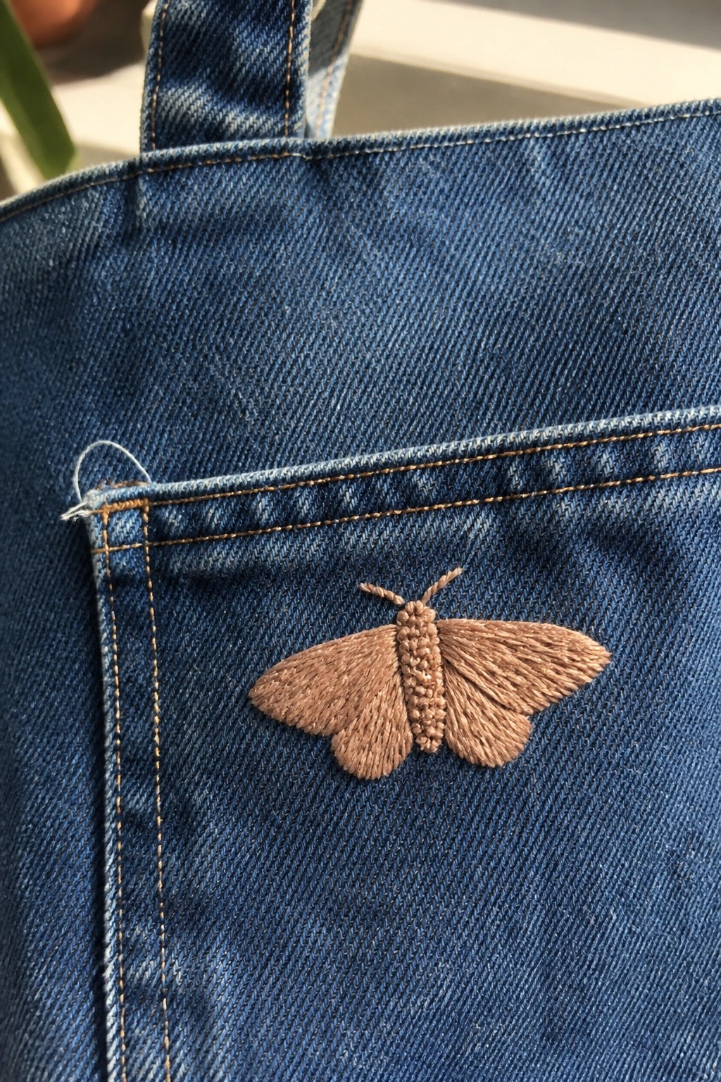 Brown embroidered moth on blue denim fabric near stitched pocket
