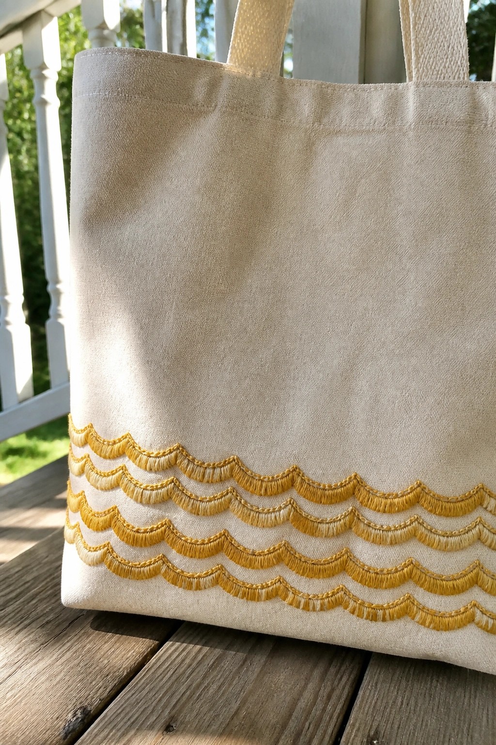 Beige canvas tote bag with yellow scalloped fringe embroidery on wooden porch