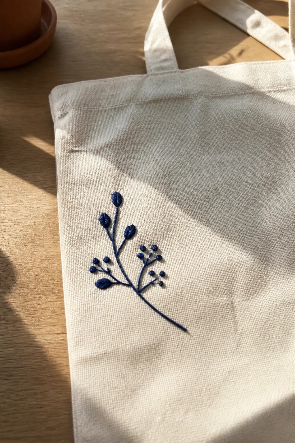 A canvas tote bag with blue embroidered branch design resting on a wooden table.