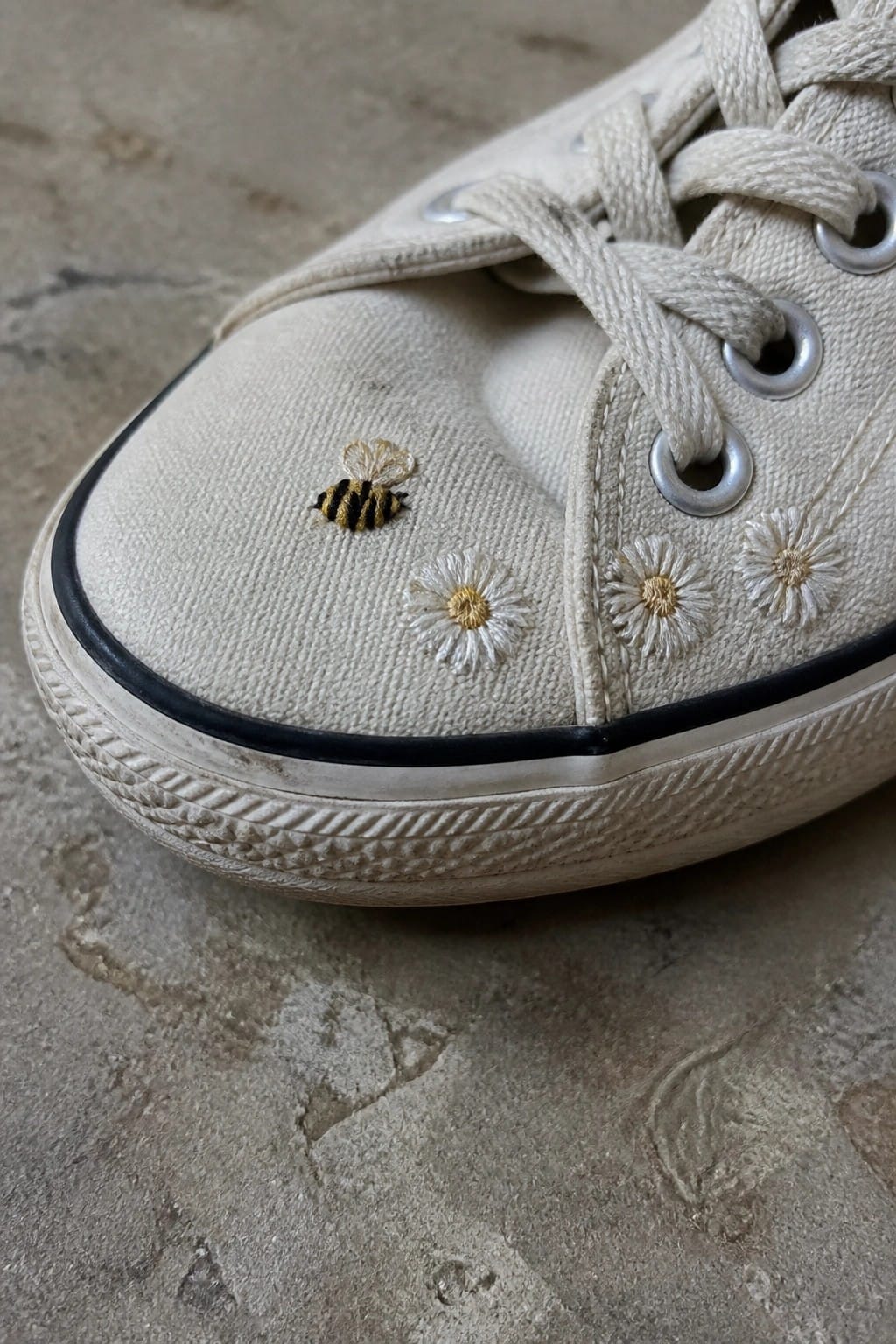 Worn white canvas sneaker with embroidered bee and daisy flowers on toe