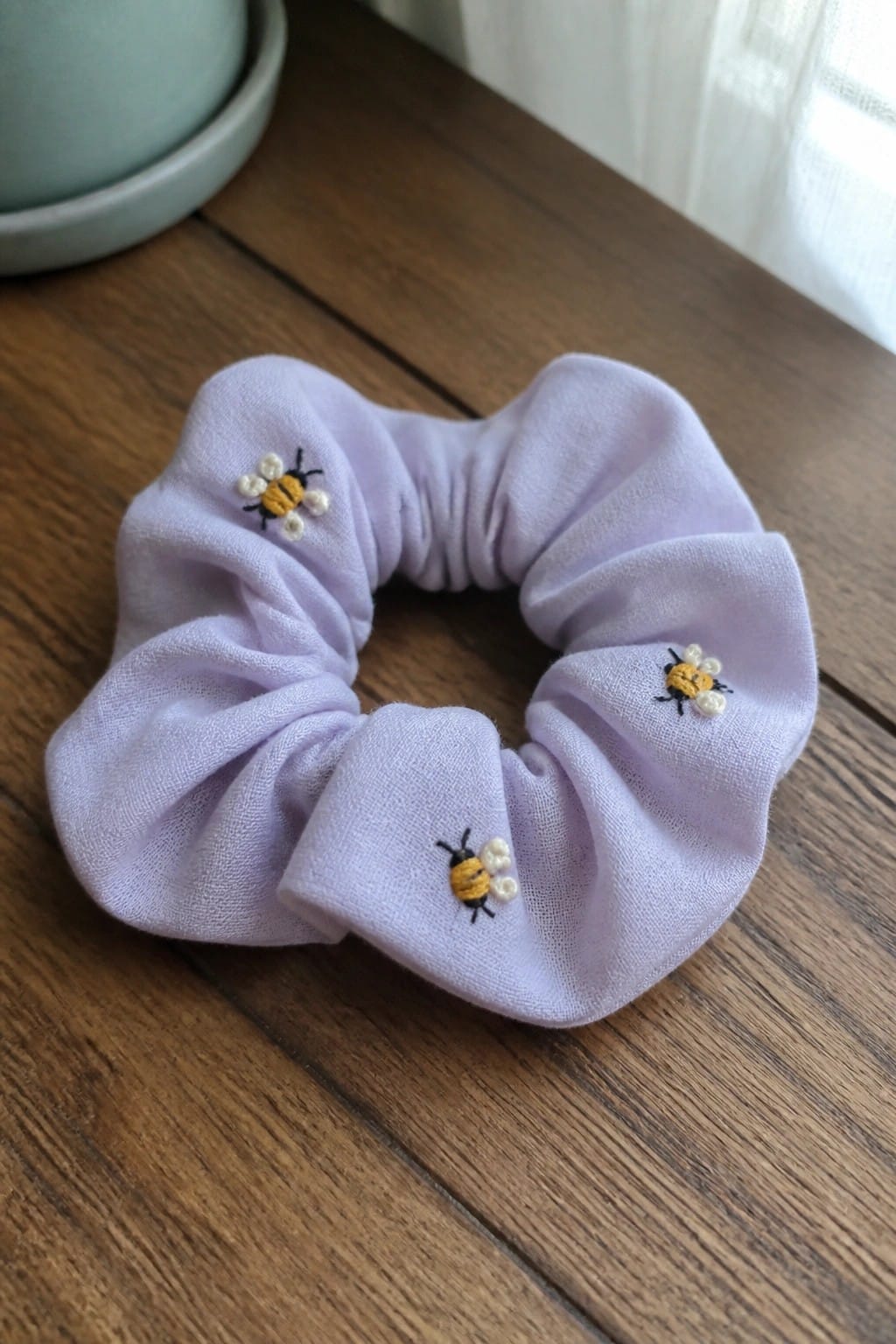 Light purple scrunchie with three embroidered bees on wooden table