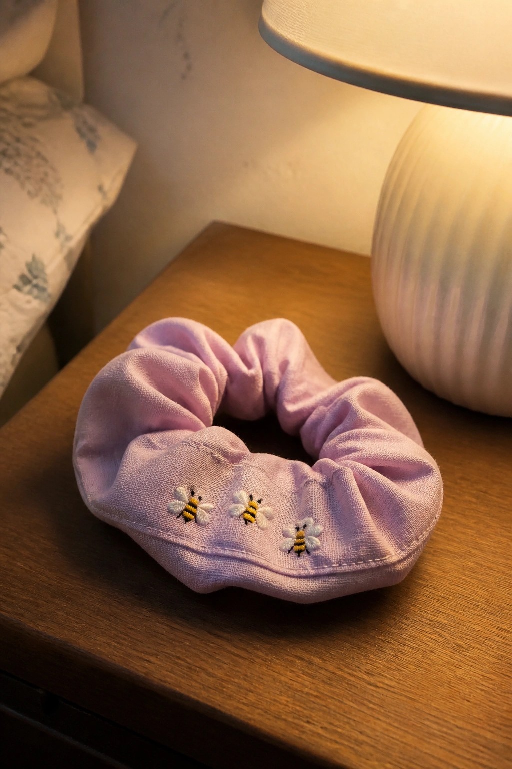 A hand holds a cream scrunchie with three small embroidered bees spaced around the band.