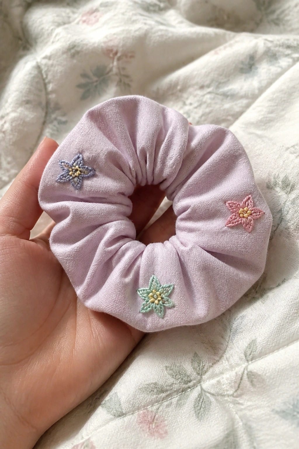 Hand holding lavender scrunchie with purple, pink, and green embroidered flowers