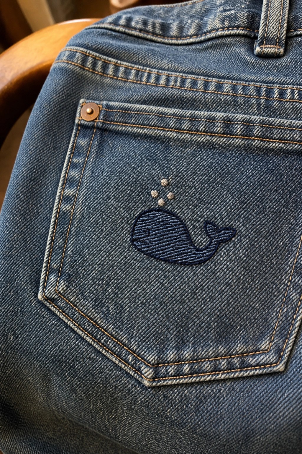 A dark blue embroidered whale with small bubbles on the back pocket of blue jeans.