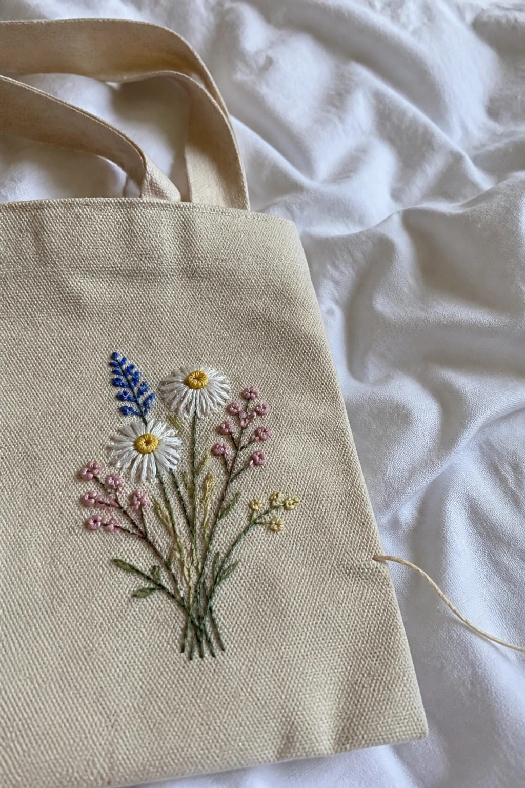 Beige canvas tote bag with embroidered cat face on brown couch