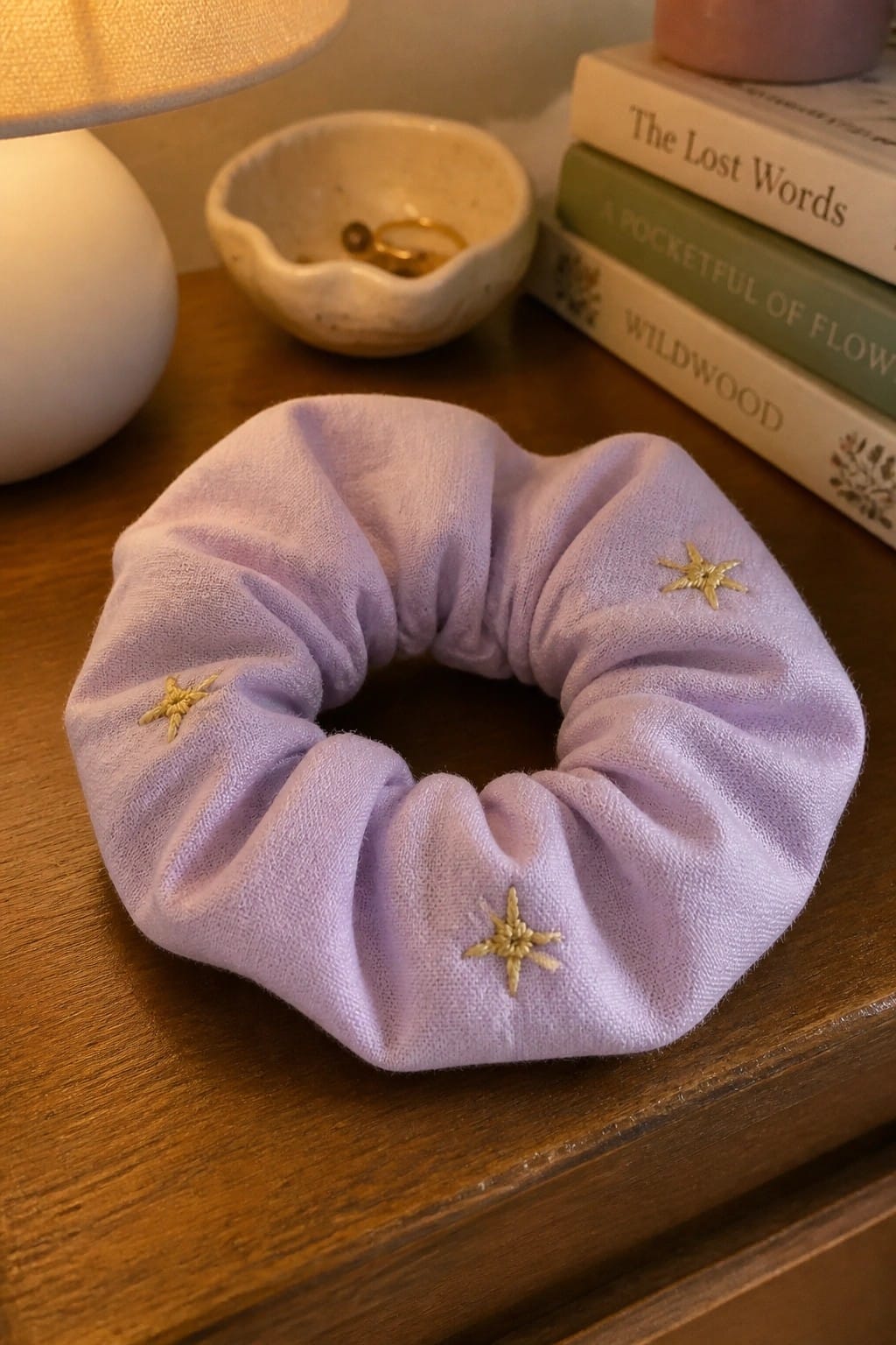 A light purple scrunchie with three small gold embroidered stars rests on a wooden table.