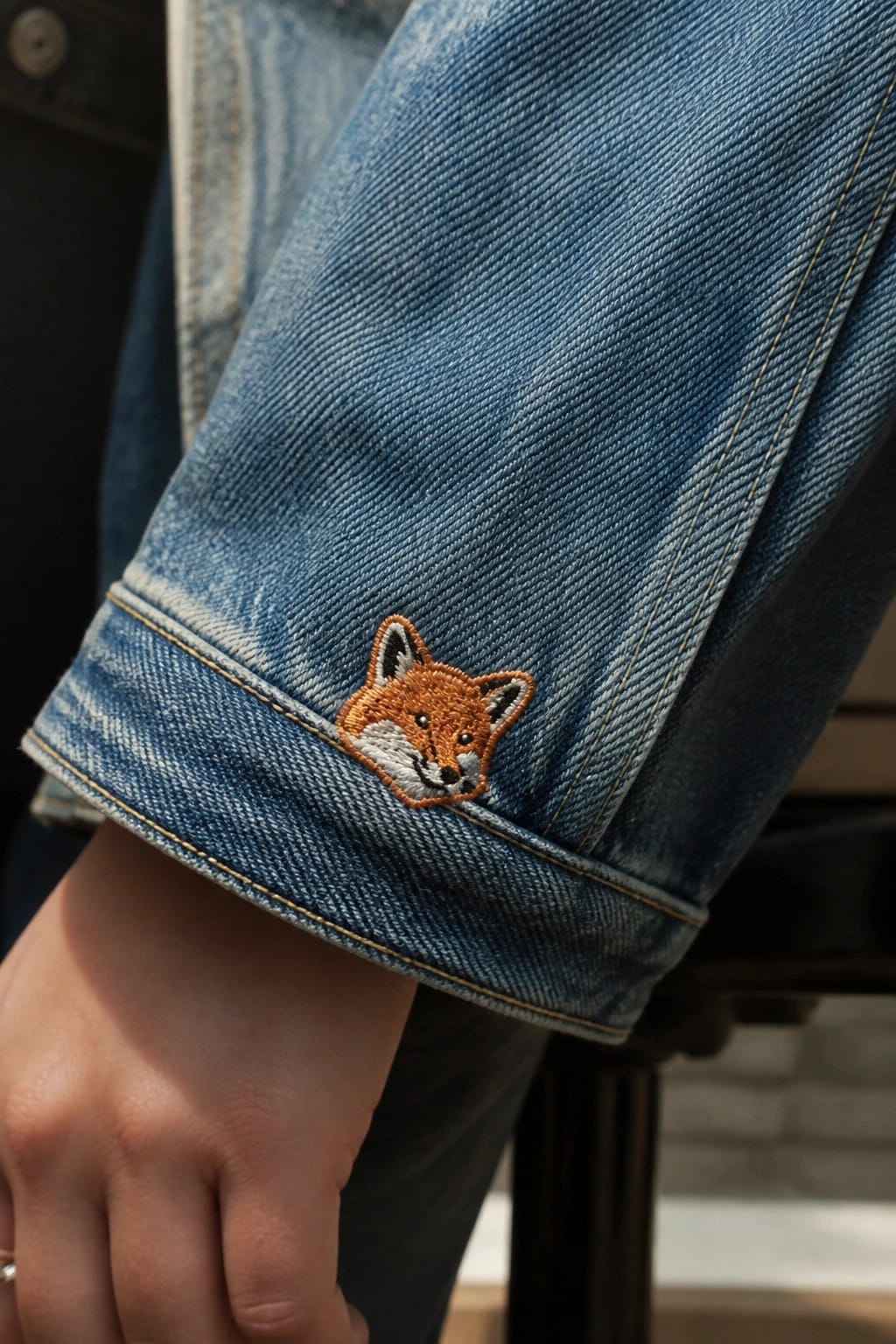 Blue denim jacket cuff with orange embroidered fox near ringed hand