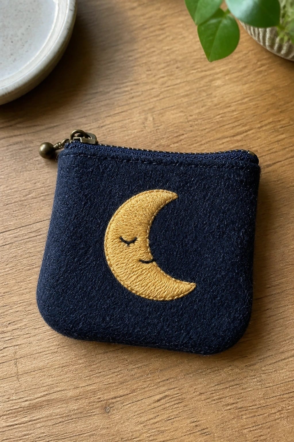 A blue denim baseball cap with white embroidered moon phases along the brim resting on a wooden chair.