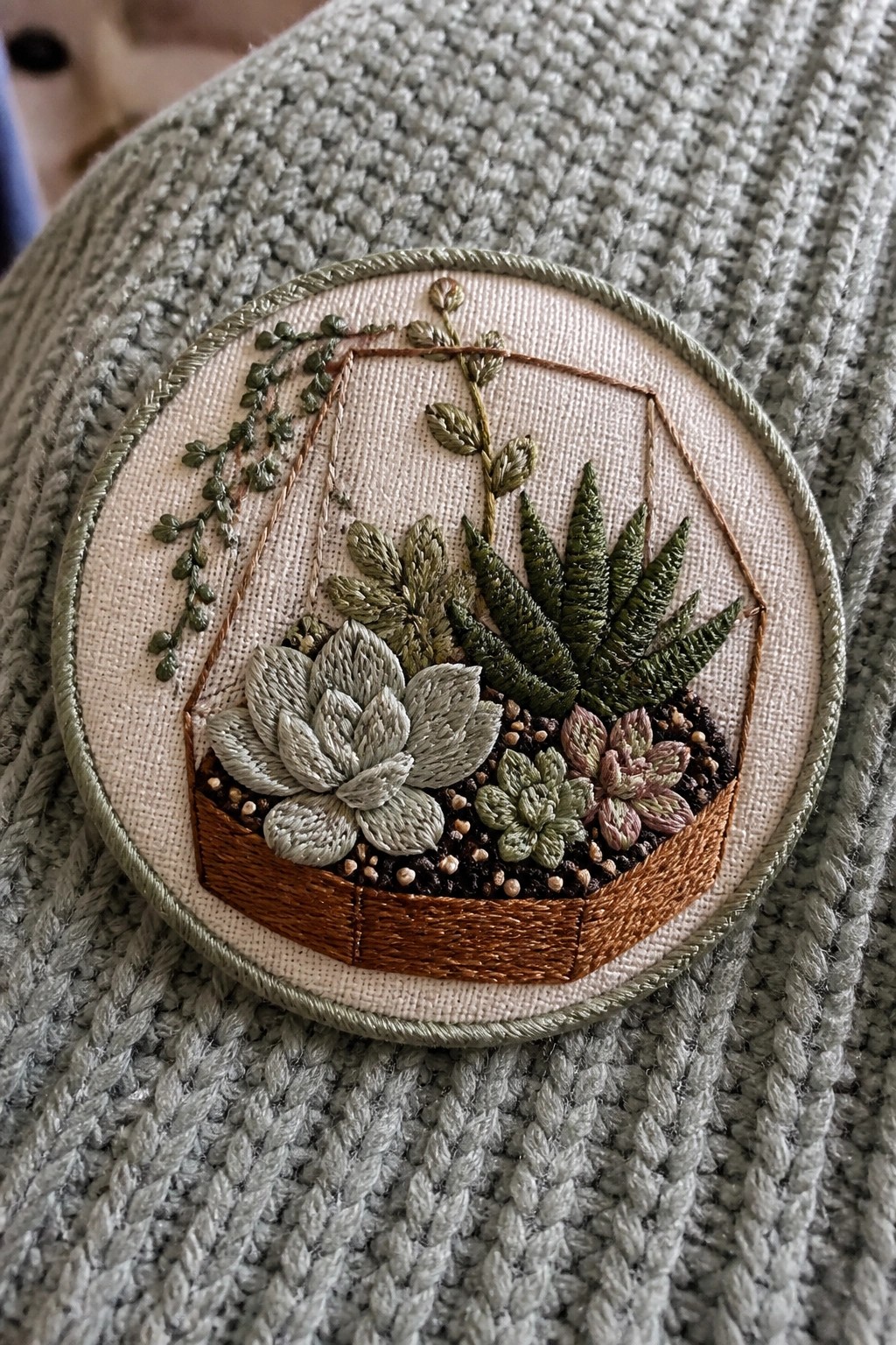 Succulent embroidery in hanging planter inside hoop on gray knit sweater
