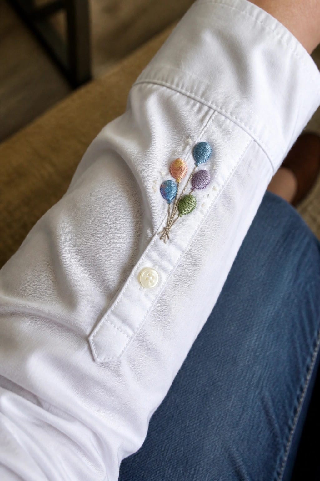 White shirt cuff embroidered with a cluster of five small colorful balloons above a button.