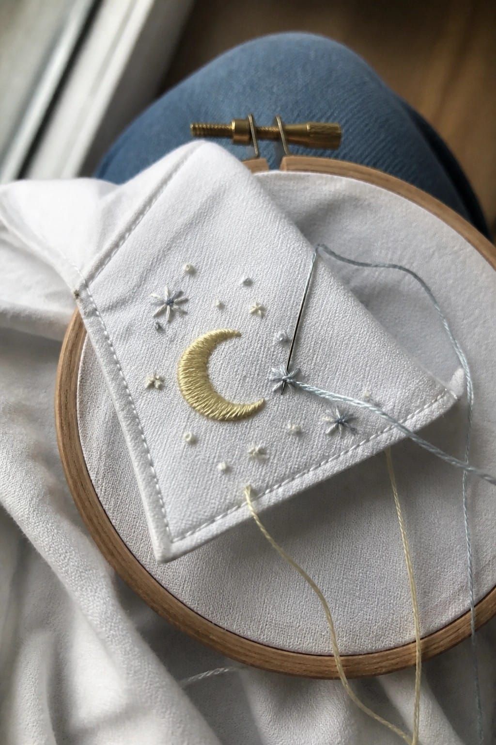 Wooden embroidery hoop with golden moon and stars on white fabric over blue jeans