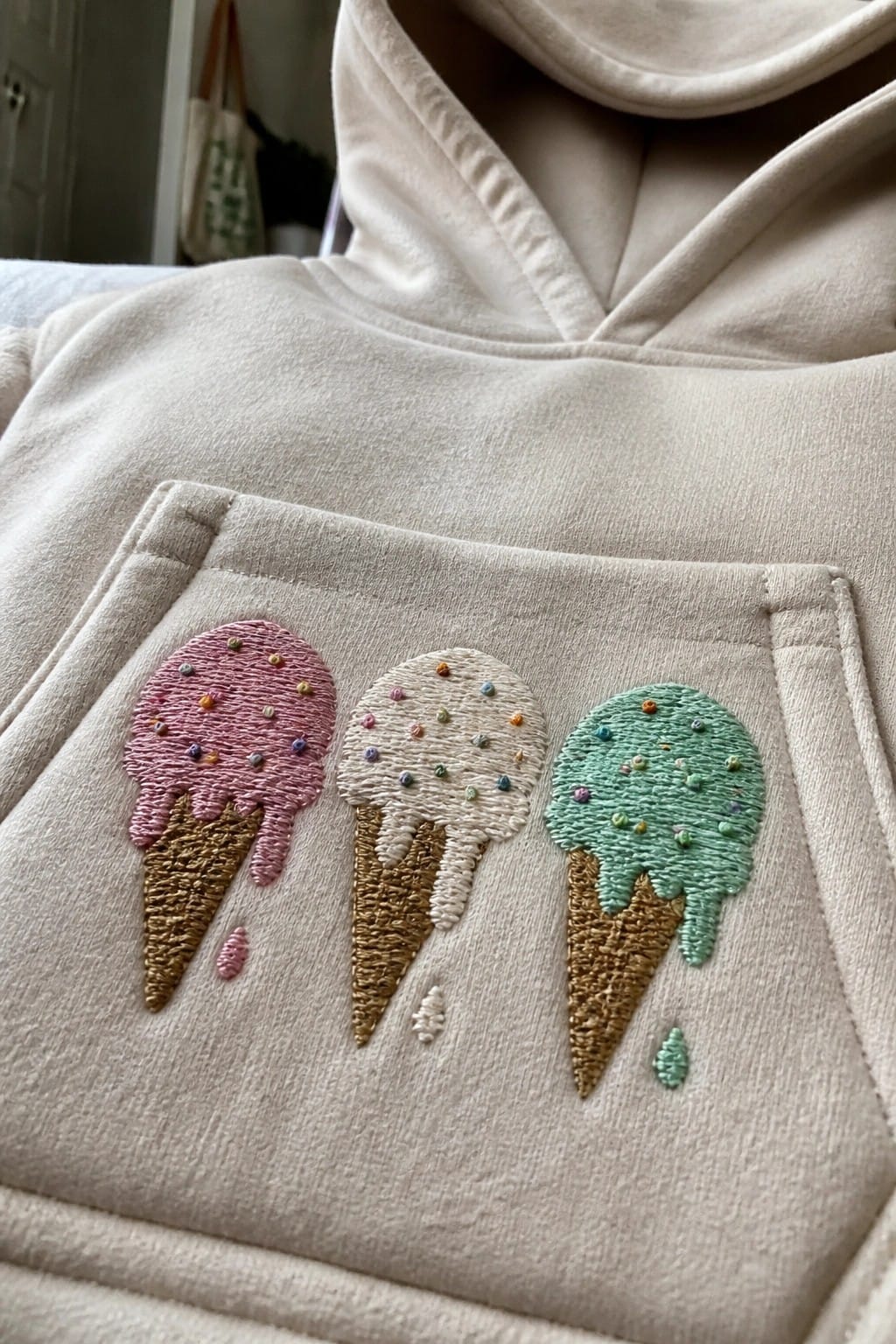 Cream hoodie pocket embroidered with three melting ice cream cones and sprinkles