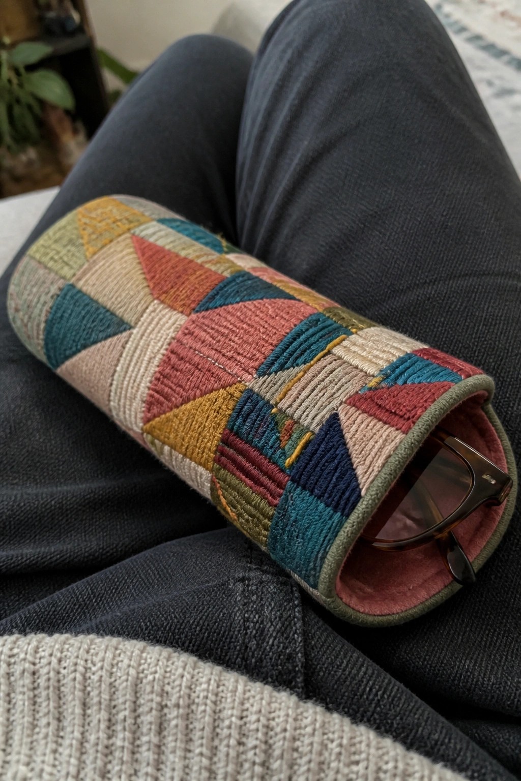 Quilted colorful geometric case with sunglasses on denim jeans lap