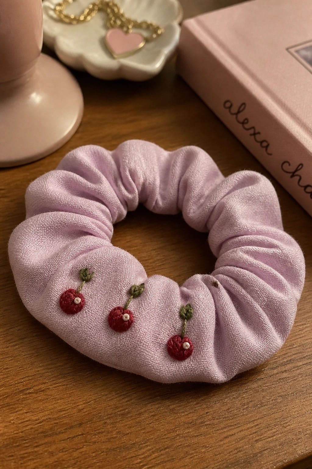 Hand holding cream satin scrunchie embroidered with three white daisies.