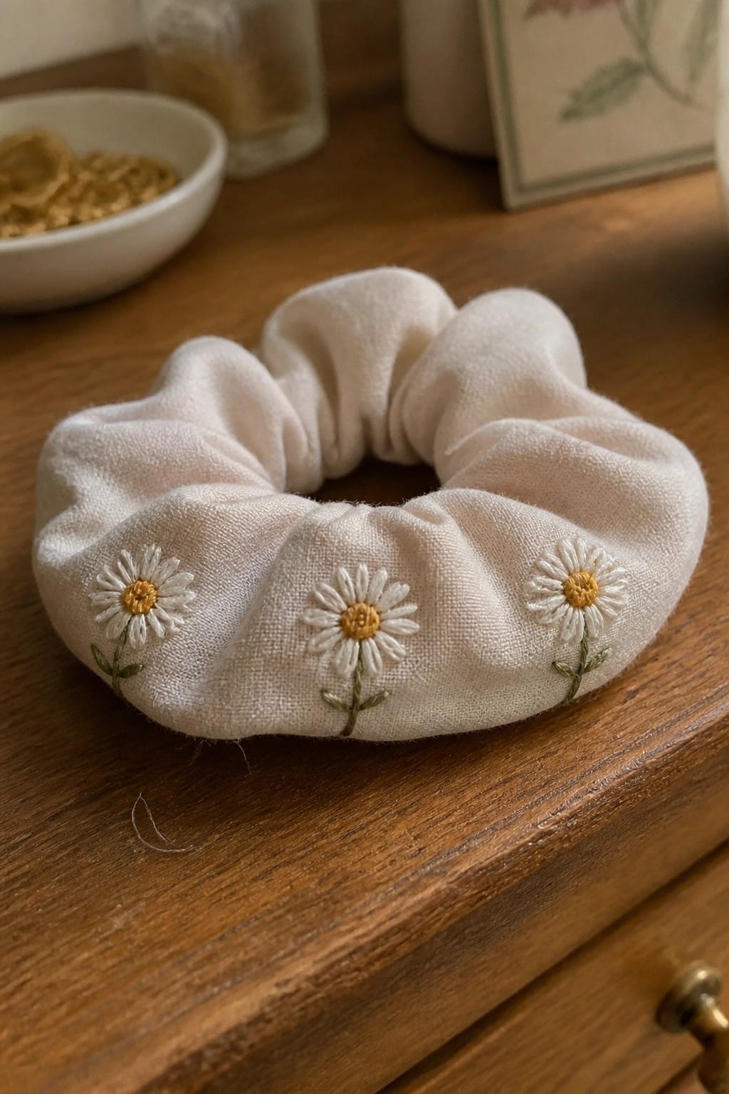 White scrunchie with three embroidered daisies on wooden dresser surface