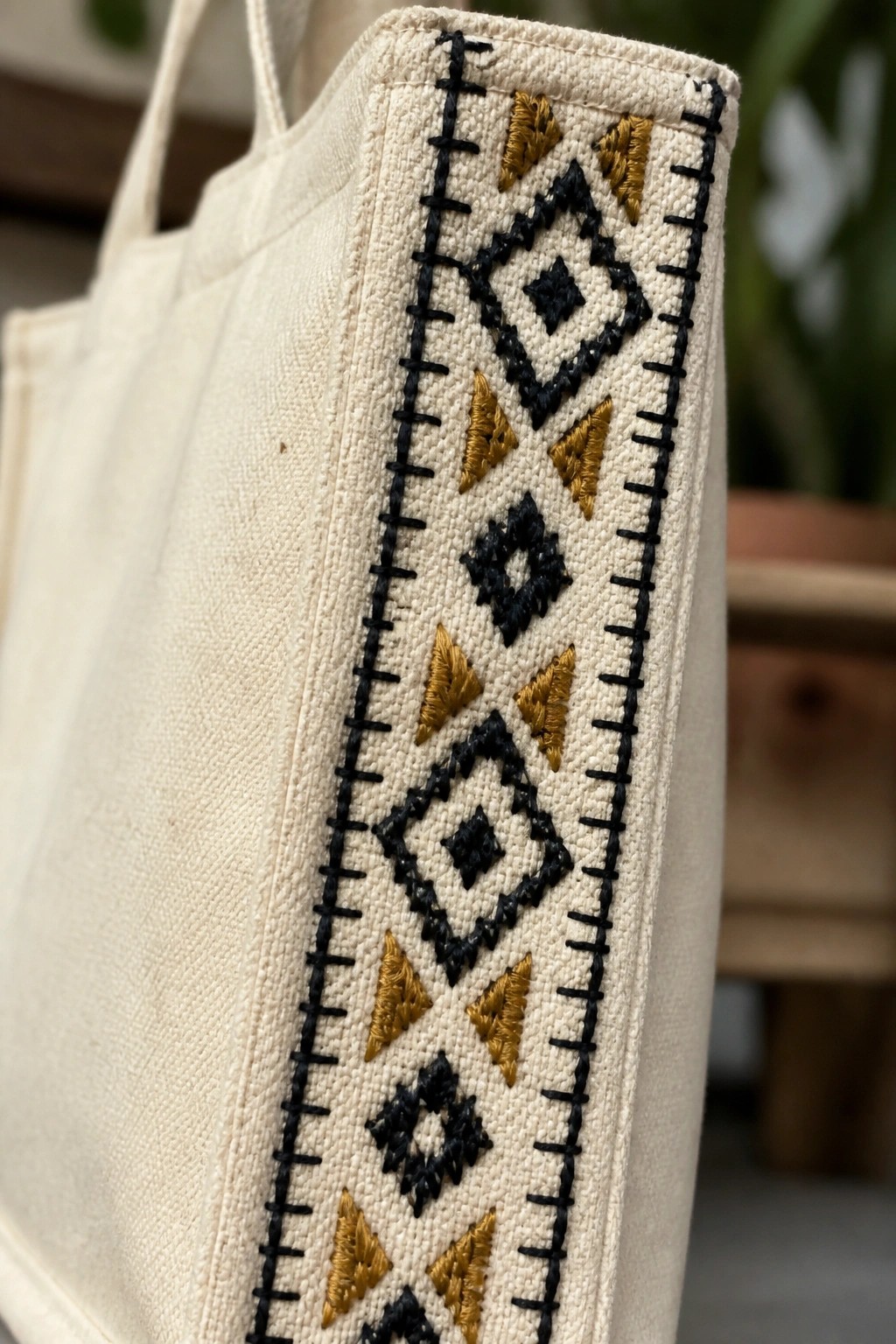 Close-up of off-white canvas tote with vertical black and gold diamond and triangle embroidery bordered by black stitching.