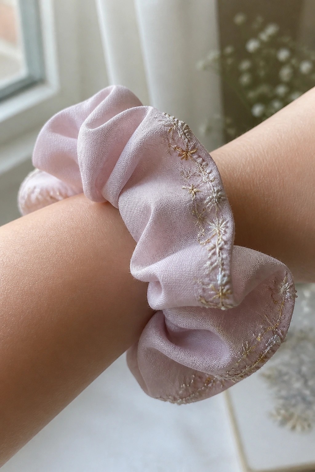 Light pink satin scrunchie with gold snowflake embroidery on a wrist