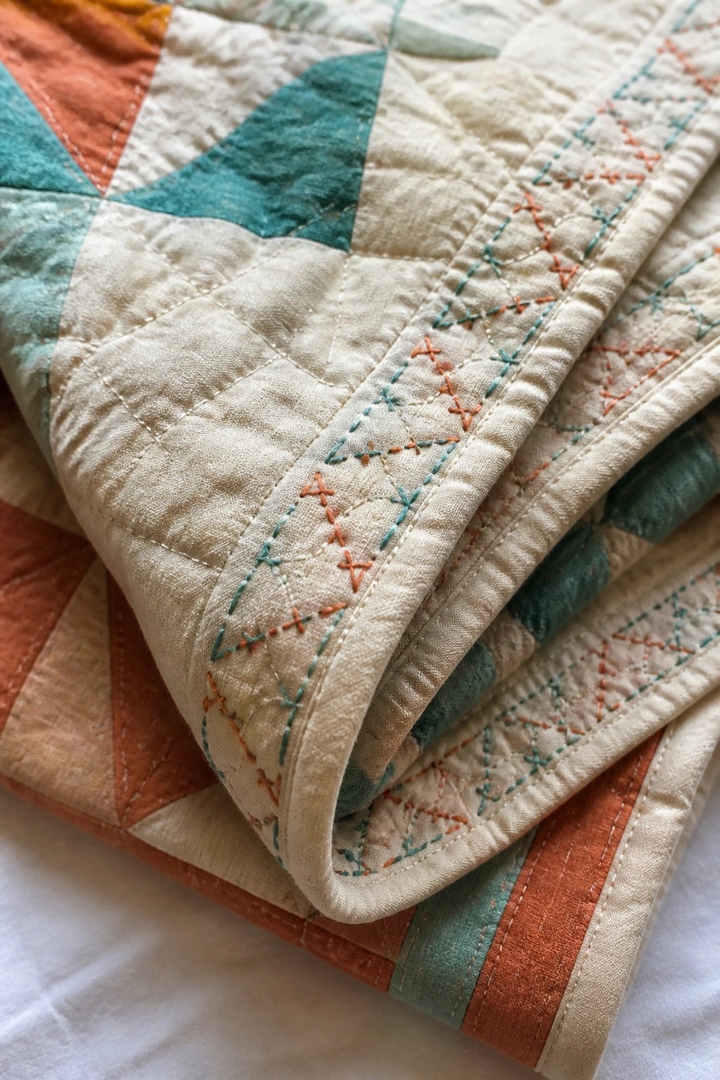 Close-up of cream quilt border with rows of small orange and teal X-stitches and dashed lines beside geometric quilt blocks.