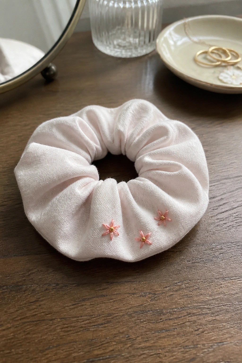 Light pink scrunchie with embroidered flowers on dark wooden table