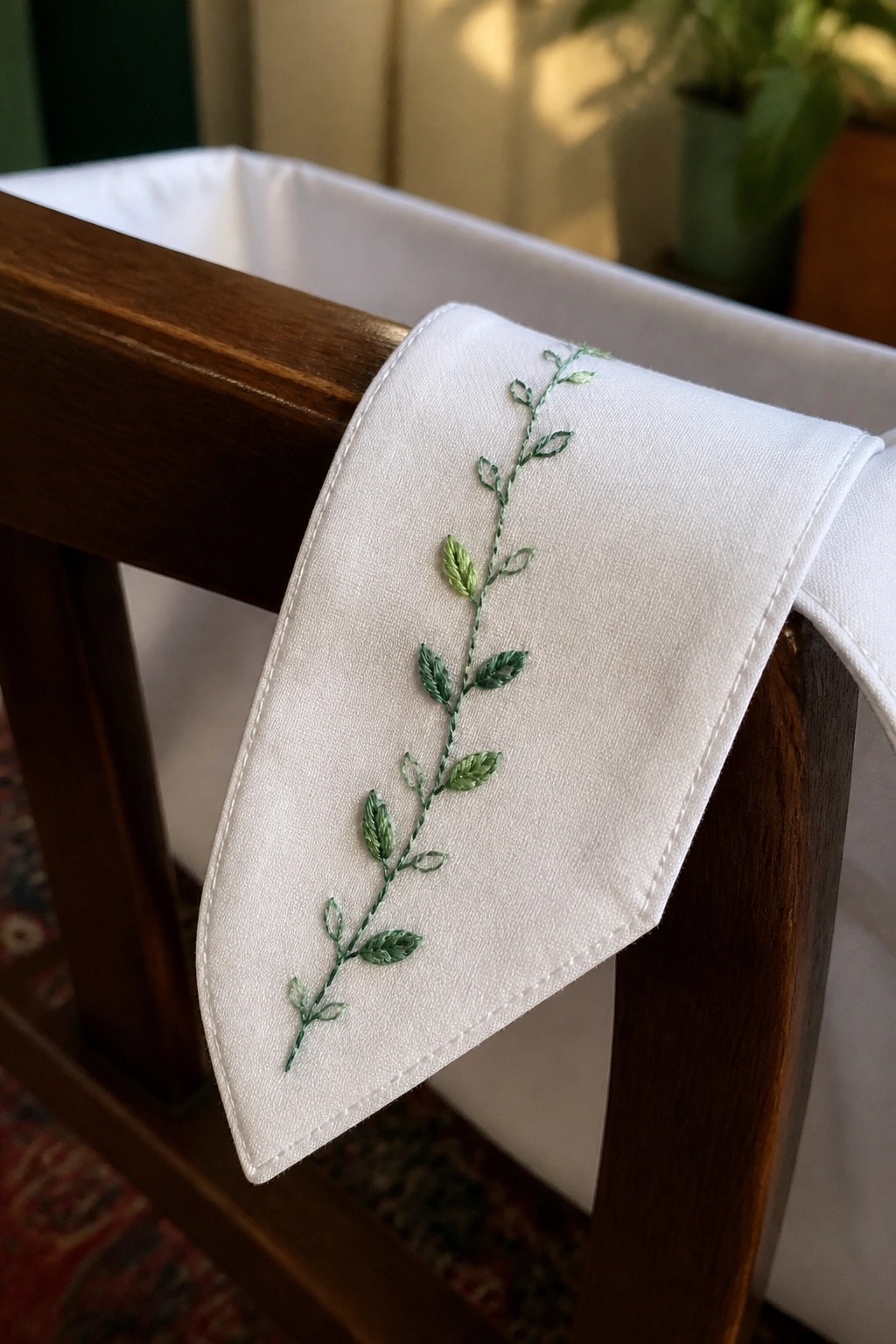 White fabric with green vine embroidery draped over wooden chair.