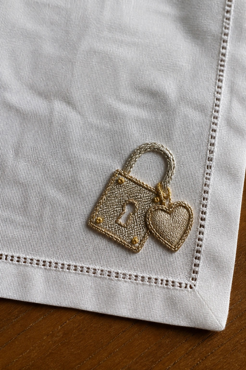 Close-up of white fabric corner with embroidered gold handbag, heart charm, and number 21.