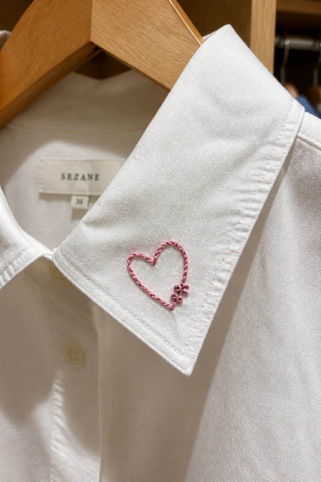 White collared shirt with pink heart and flower embroidery on wooden hanger