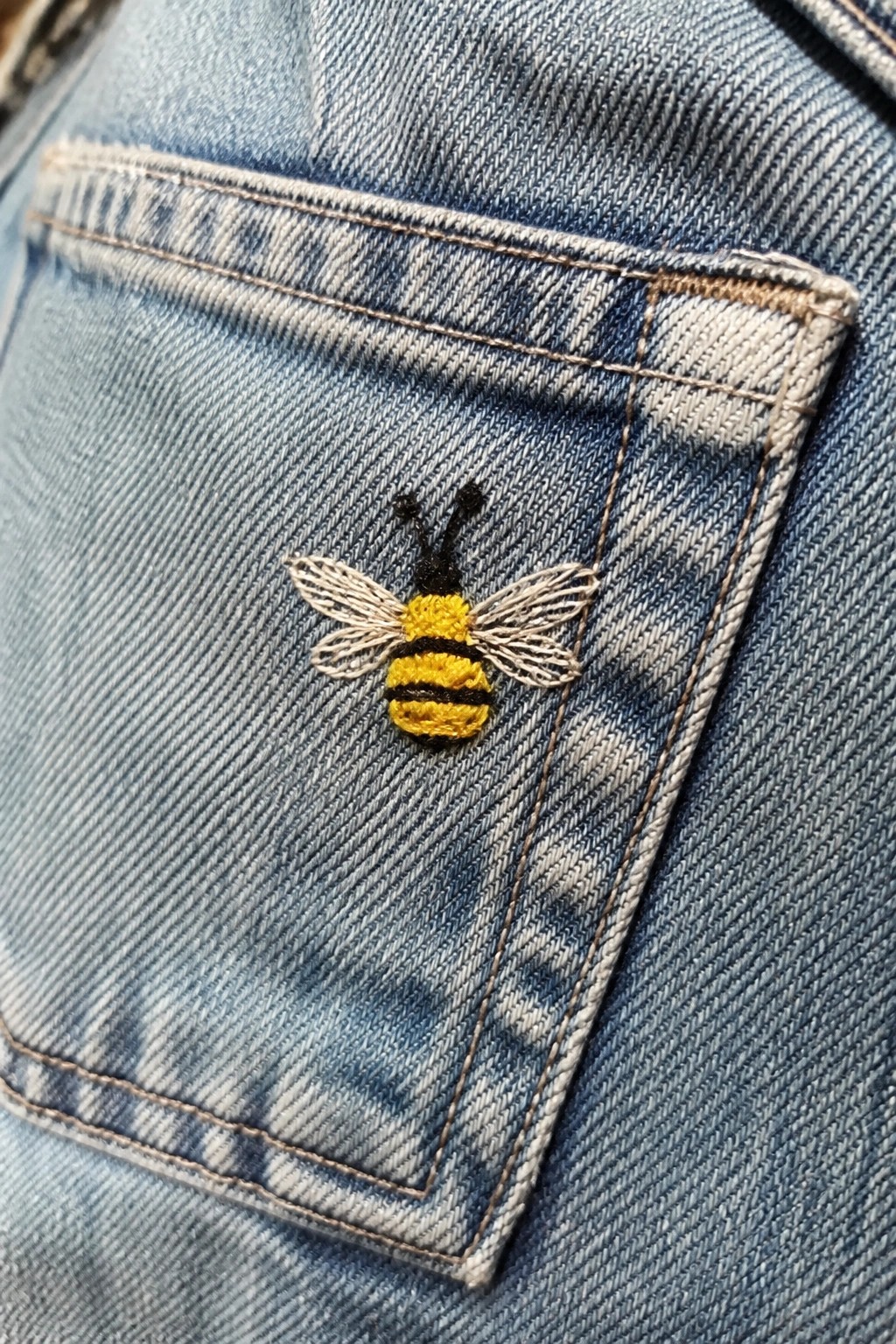Embroidered yellow and black bee on the pocket of blue denim jeans.