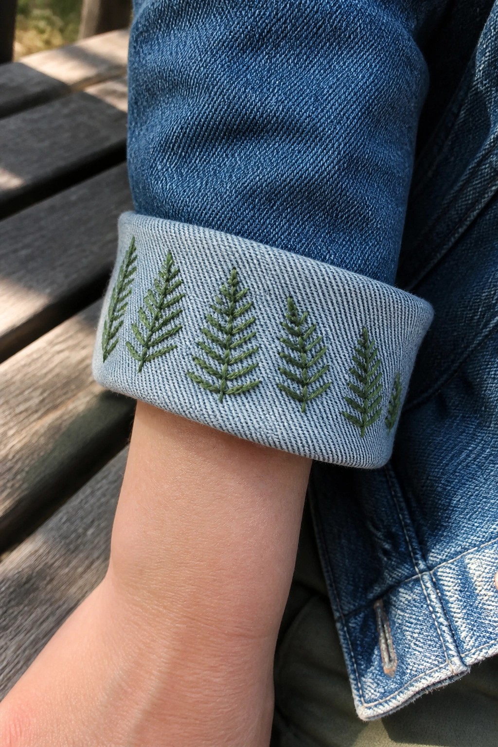 Green embroidered fern patterns on the light blue cuff of a blue denim jacket.