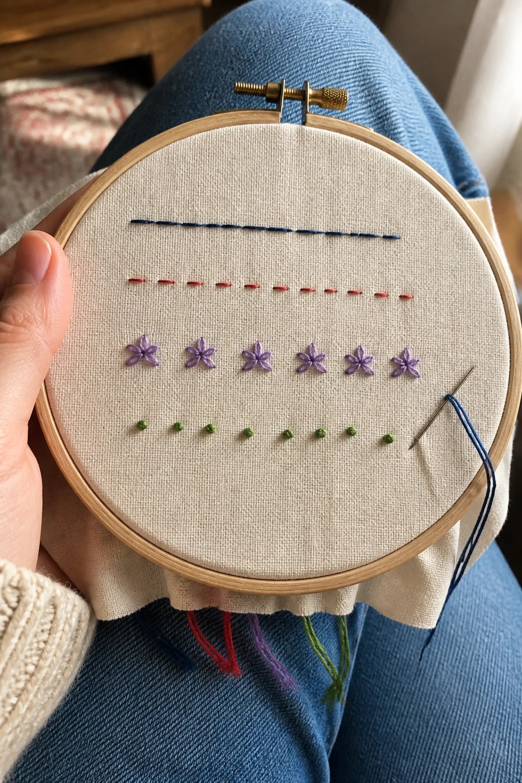 Hand holding embroidery hoop with blue, red, purple flower, and green stitches on fabric