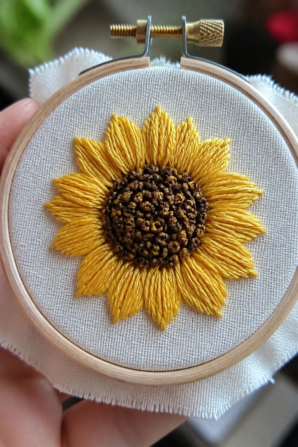 Hand holding wooden hoop with yellow sunflower embroidery on white fabric
