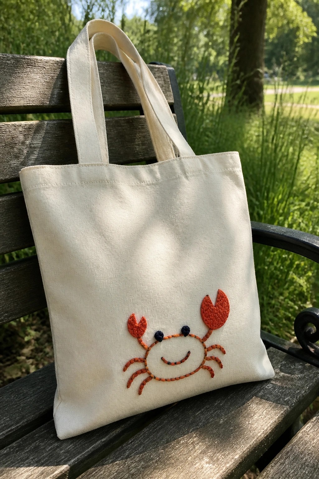 Cream tote bag with orange embroidered crab on wooden park bench outdoors