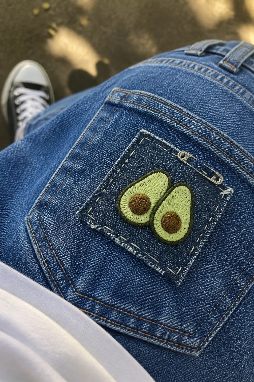 Blue denim jeans back pocket with embroidered avocado patch and safety pin.