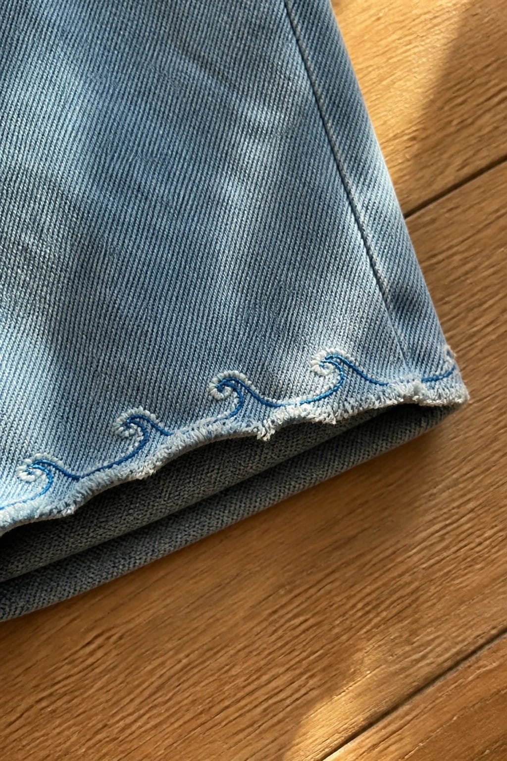 Light blue denim jeans with pink embroidered bow above a frayed rip.