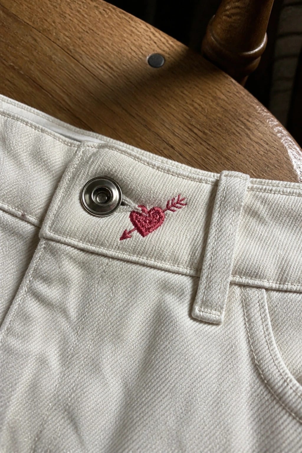 Close-up of light blue denim jeans with small red cherry embroidery on the coin pocket.