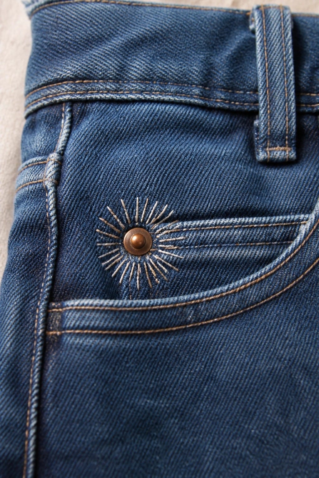 Blue denim jeans waistband with embroidered compass rose and Lucky Brand button