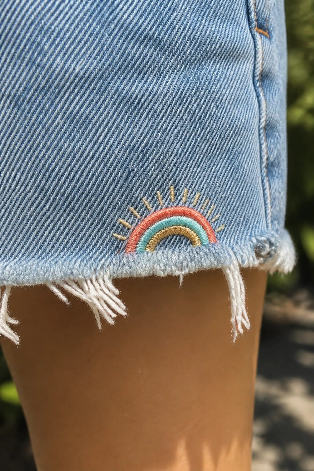 Light blue denim shorts with embroidered rainbow and sun rays on frayed hem