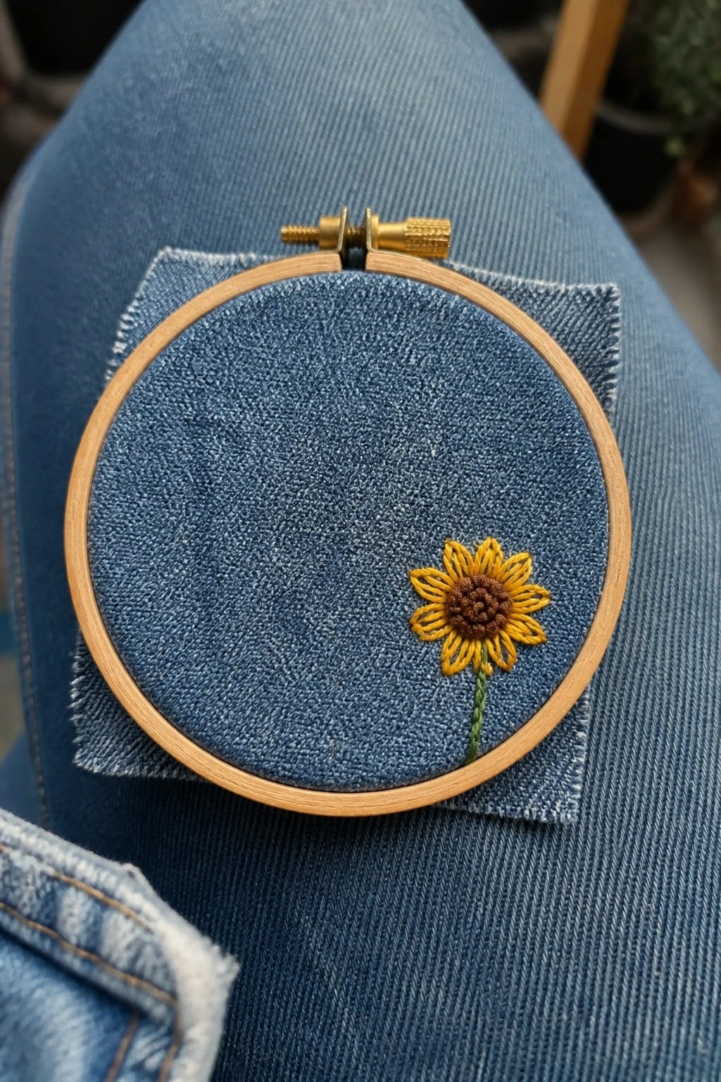 Wooden hoop with yellow sunflower embroidered on blue denim over jeans